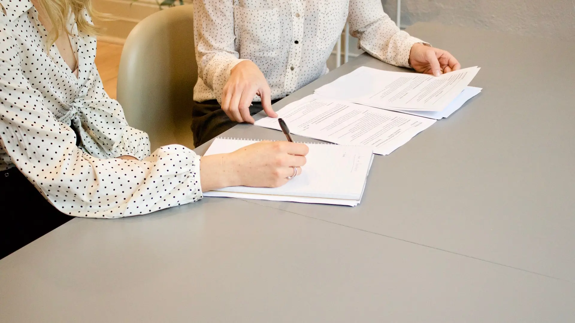 woman signing on white printer paper beside woman about to touch the documents